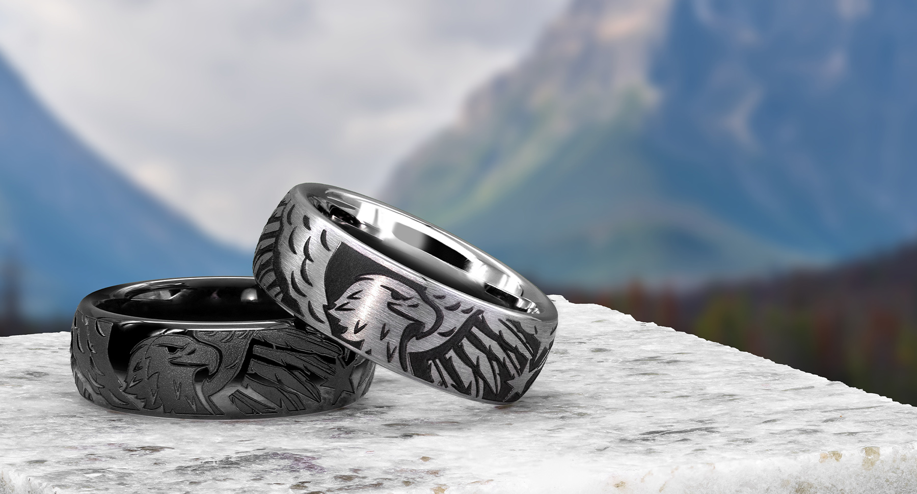 Two mens rings featuring eagle laser engraved onto them with mountains in the background.